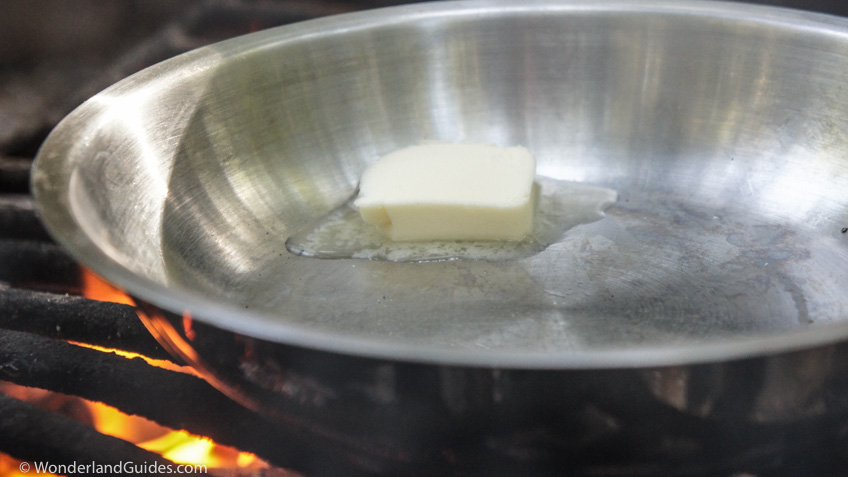 Heating a pat of butter in a pan over an open fire